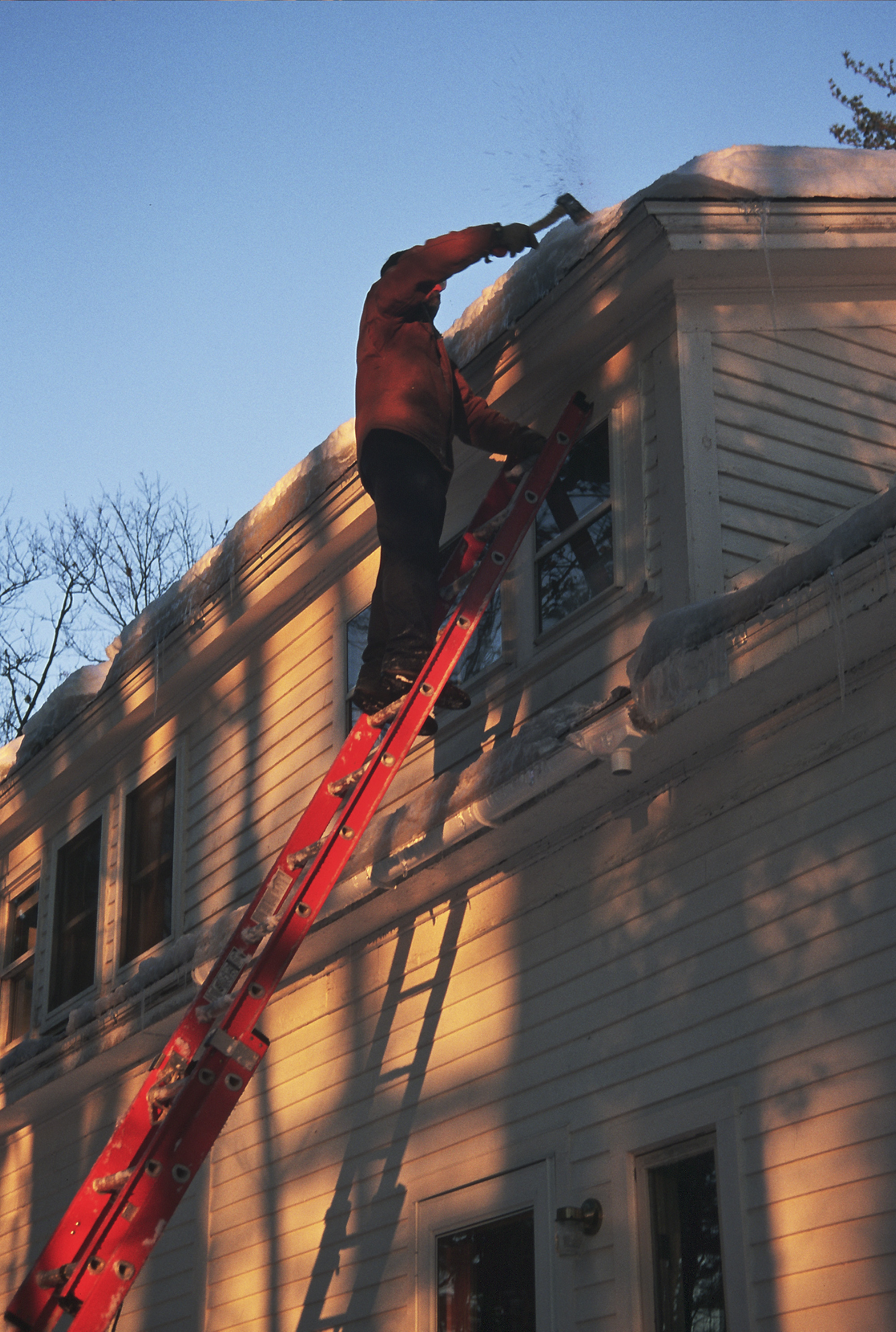 Someone on a ladder chopping ice off a roof.